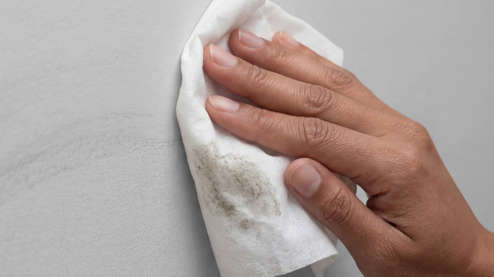 A hand wiping a wall with a white cloth to collect a dust sample