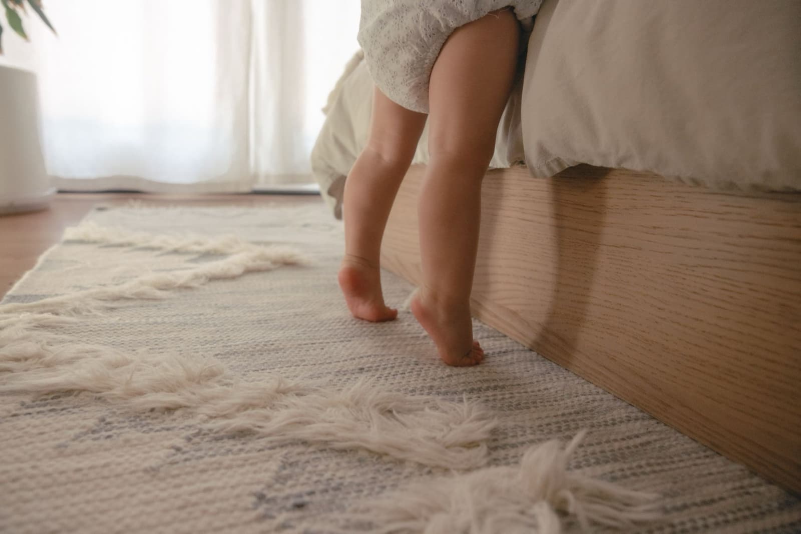 A small child standing barefoot beside a bed